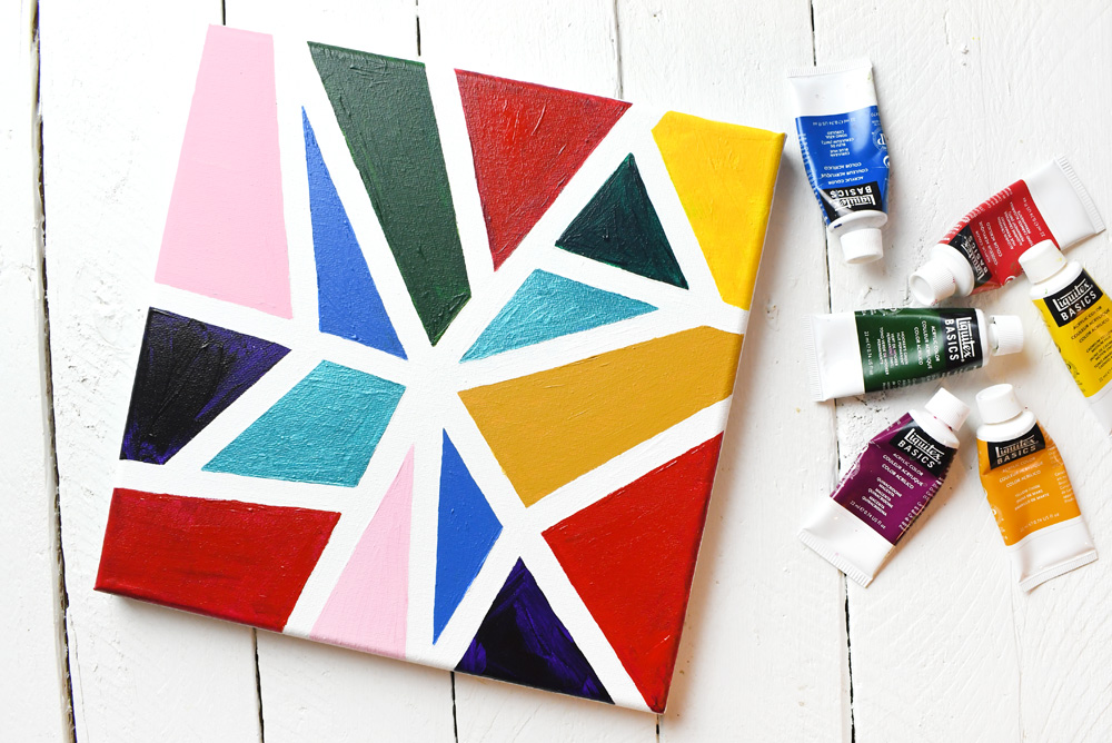A canvas with multicolored shapes painted. Used paint tubes are off to the right