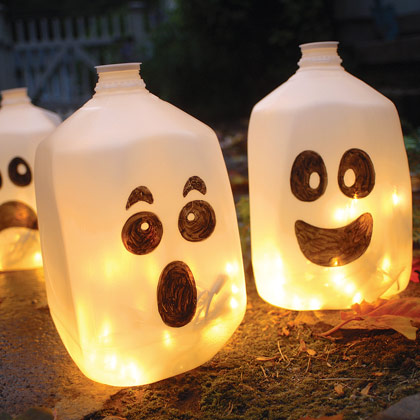 Milk jugs with black sharpie faces drawn on. The jugs are filled with lights to resemble jack-o-lanterns