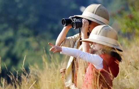 Two children outside, one is using binoculars and the other is pointing.