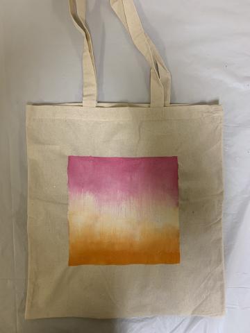 A canvas tote bag with a square, gradient design featuring orange, white, and pink colors