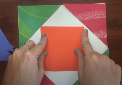 Two hands placing multi-colored paper shapes on a piece of white paper