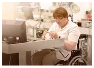 A person seated in a wheelchair works at a desk with a computer.