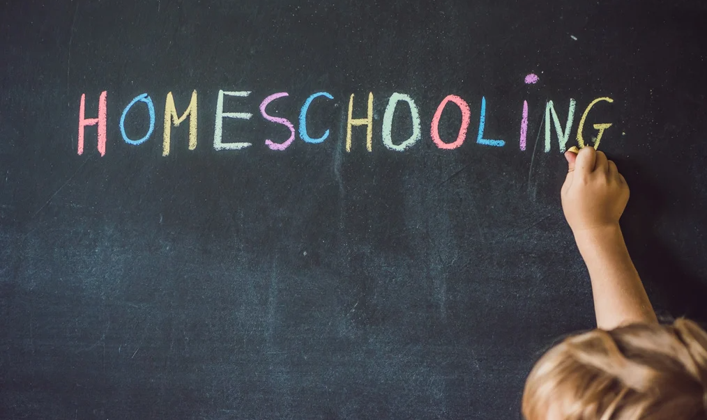 A child writes HOMESCHOOLING on a chalkboard.