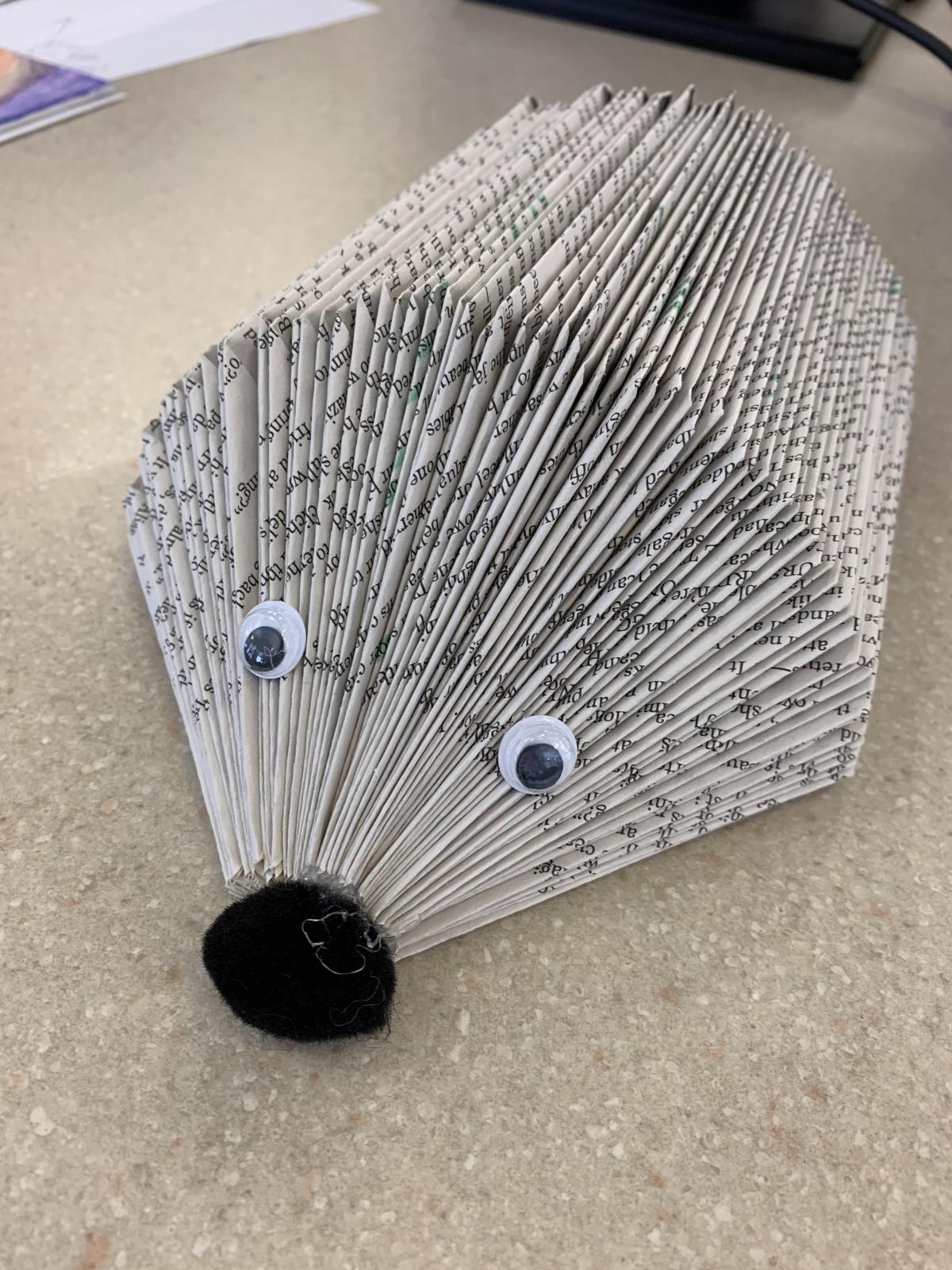 Book pages folded to resemble a hedgehog. Googly eyes and a black pom pom are attached for eyes and a nose