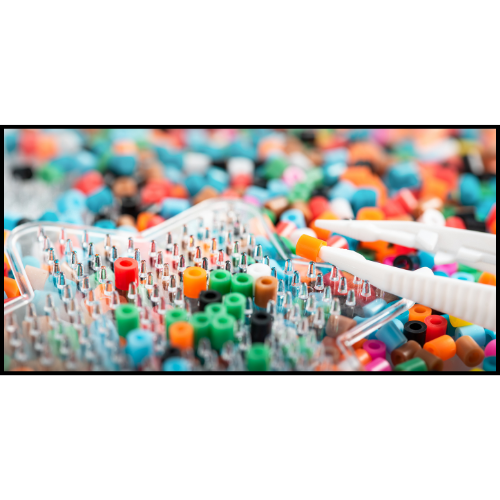 A pile of perler beads with a peg board laying on top. Tweezers are above the peg board with a single bead in them