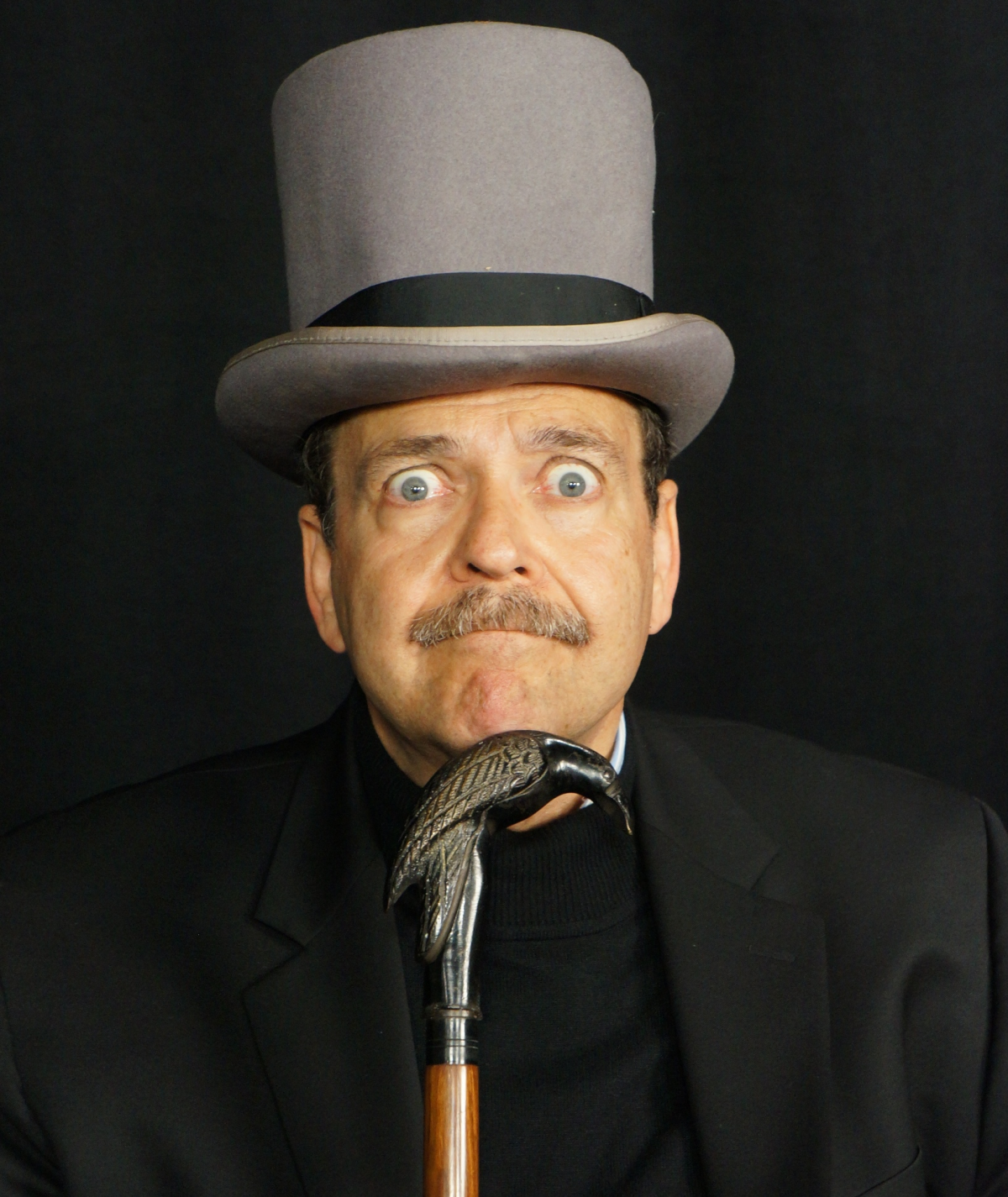 Actor in grey top hat holding a cane with a raven handle